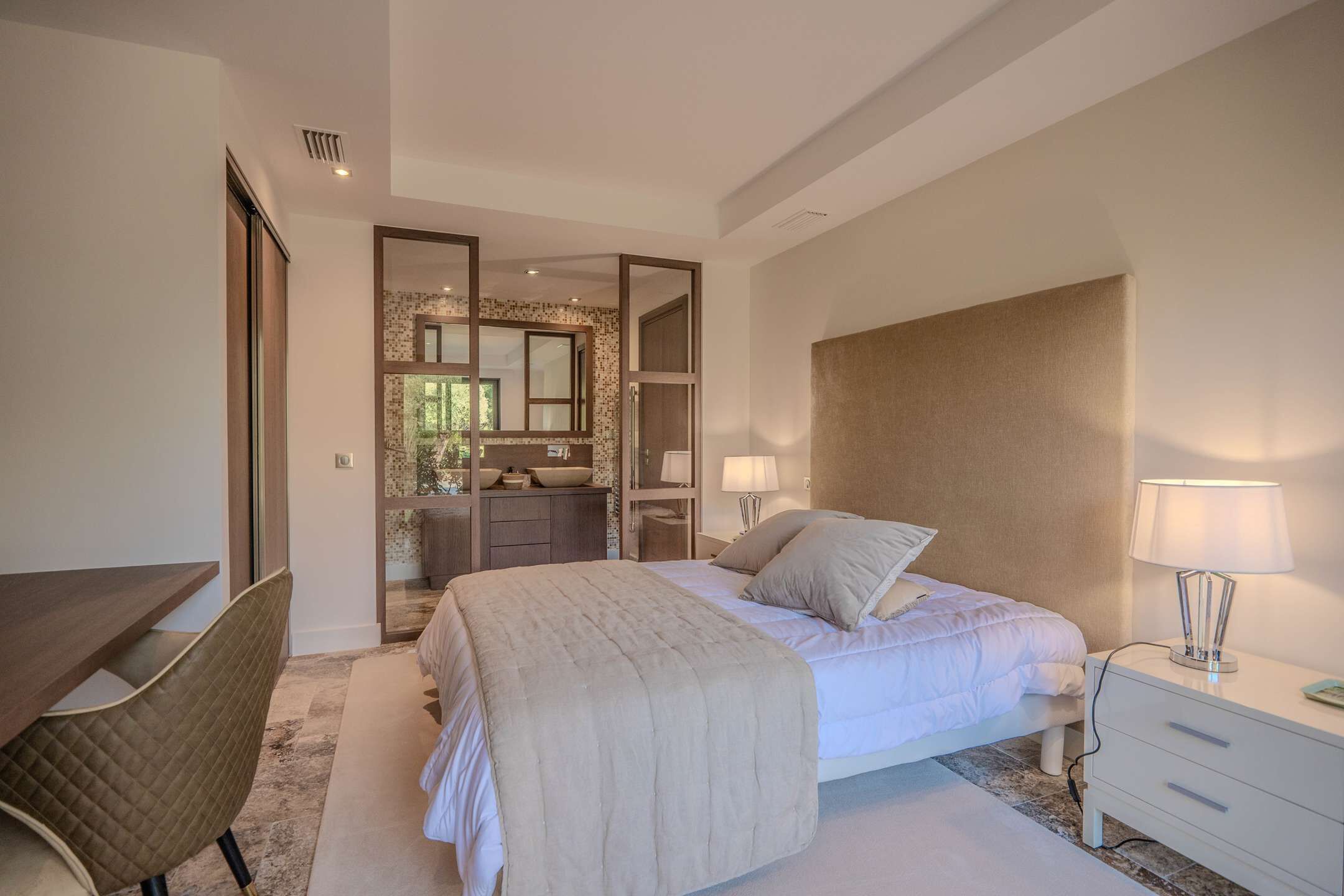 A bedroom with a bed, bedside table, lamp, and a desk with a chair.