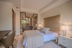 A bedroom with a bed, bedside table, lamp, and a desk with a chair.