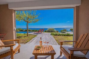 A wooden table with a bottle and glasses, two chairs, and a view of a pool and beach through a glass door. - LES ISSAMBRES - SEA FRONT AMAZING VILLA WITH SWIMMING-POOL (LES ISSAMBRES)