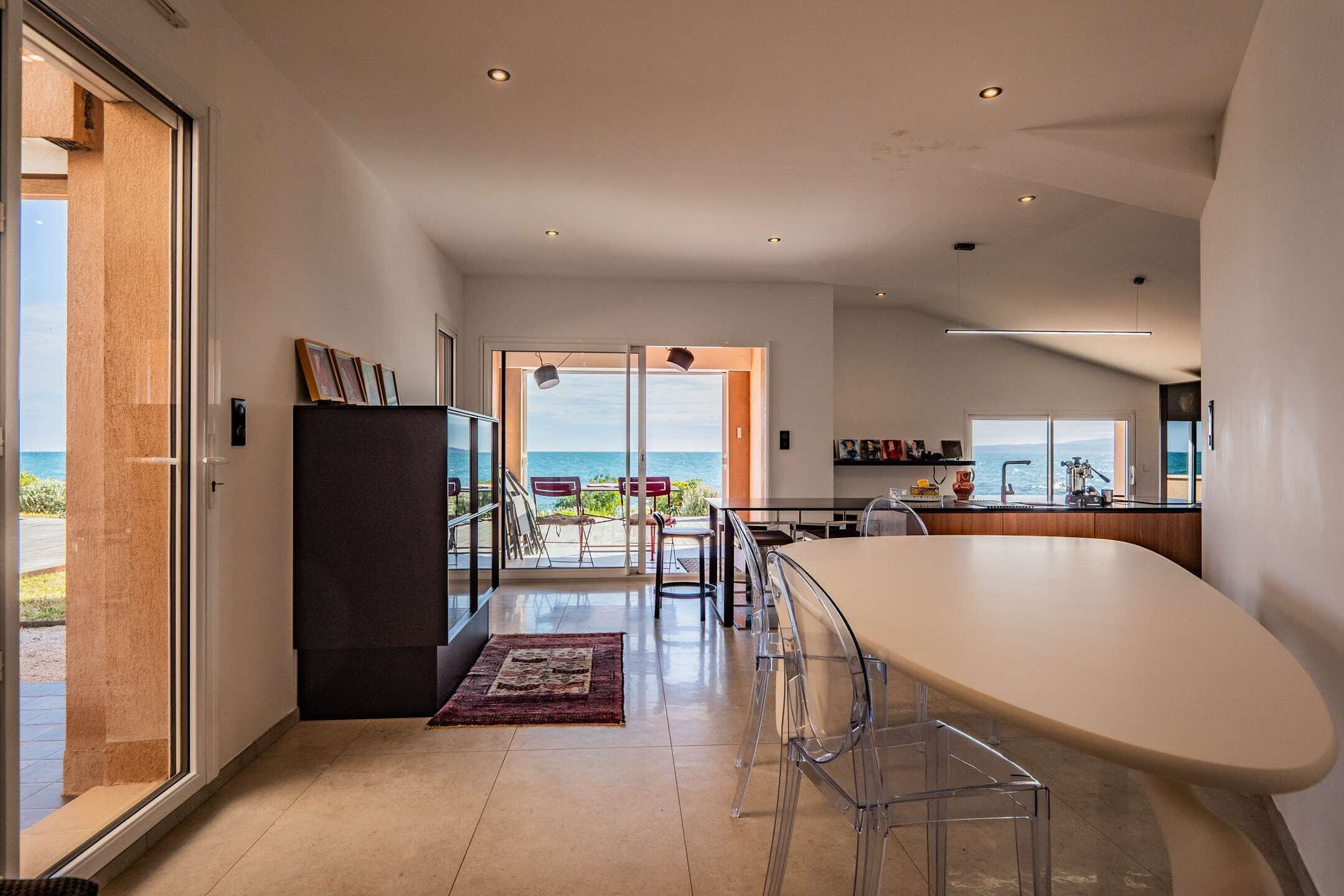 Een moderne keuken met een groot kookeiland, een eethoek met stoelen en uitzicht op de oceaan.