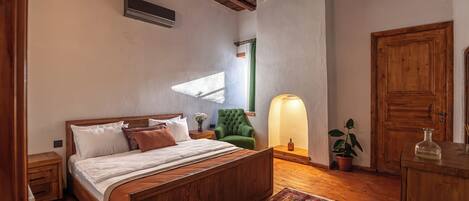 Een slaapkamer met een houten bed, een groene fauteuil, een nachtkastje, een lamp, een kamerplant en een houten garderobe.
