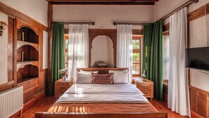 A wooden-framed bedroom with a bed, nightstands, a TV, and a window with curtains. - Marassa Konak Otel (Ermenek)