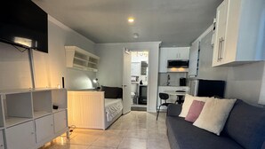 Una sala de estar moderna con un sofá, un televisor y una cocina al fondo.