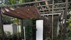 Un patio empedrado con una pérgola, una puerta blanca y abundante vegetación.