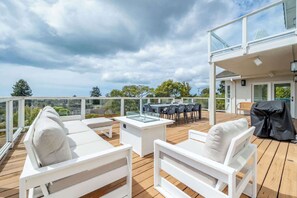 Una terraza con mobiliario blanco, una mesa de vidrio y una parrilla.