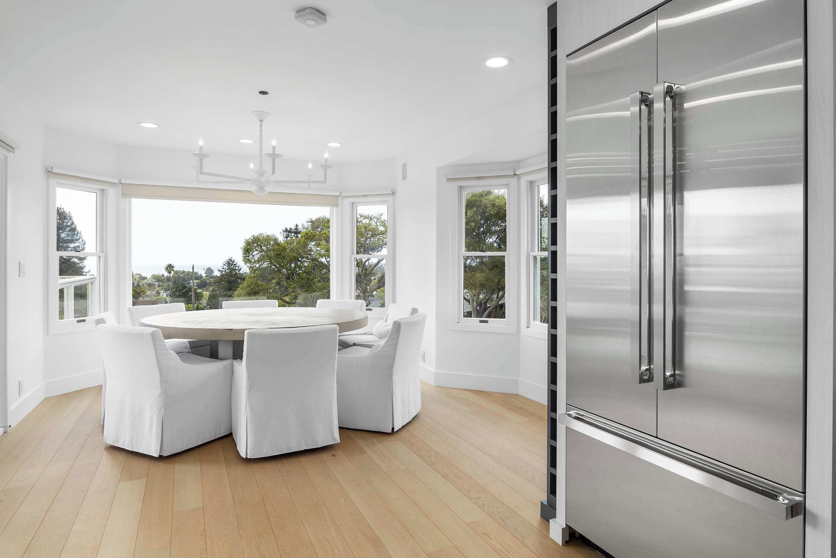 Une cuisine moderne dotée d’un réfrigérateur en acier inoxydable, de meubles blancs et d’un coin repas avec une table ronde et des chaises blanches.