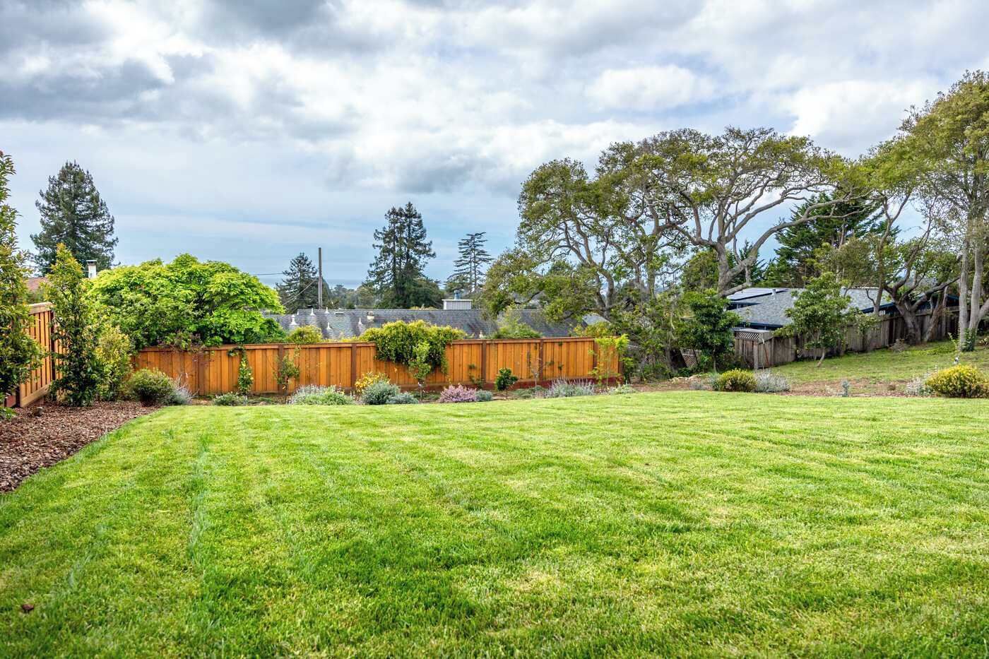 A well-maintained backyard with a wooden fence, various shrubs, and a lawn.