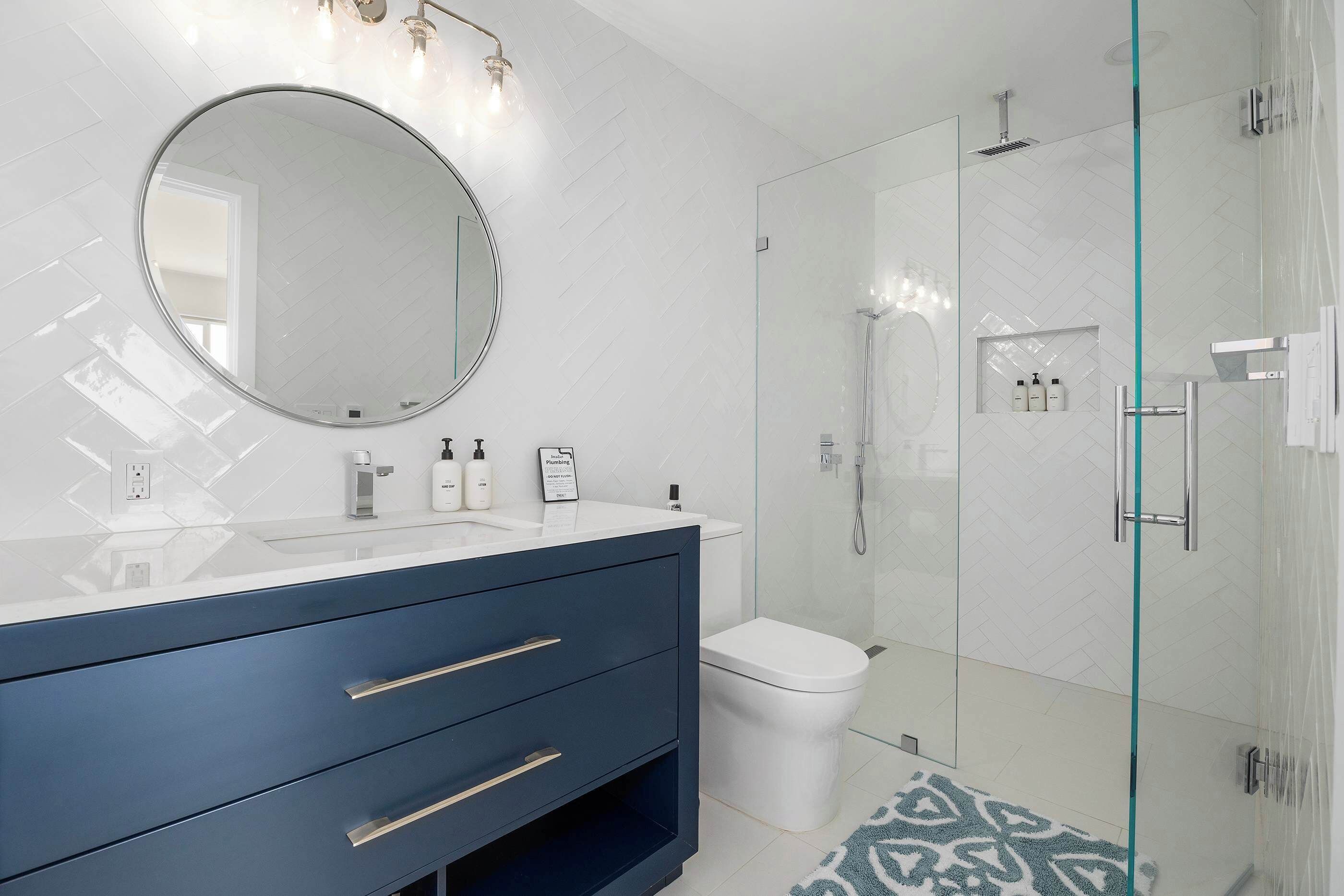Une salle de bain moderne avec une douche à parois de verre, un miroir rond et un meuble-lavabo avec des tiroirs.