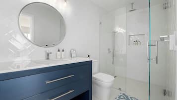 Une salle de bain moderne avec une douche à parois de verre, un miroir rond et un meuble-lavabo avec des tiroirs.