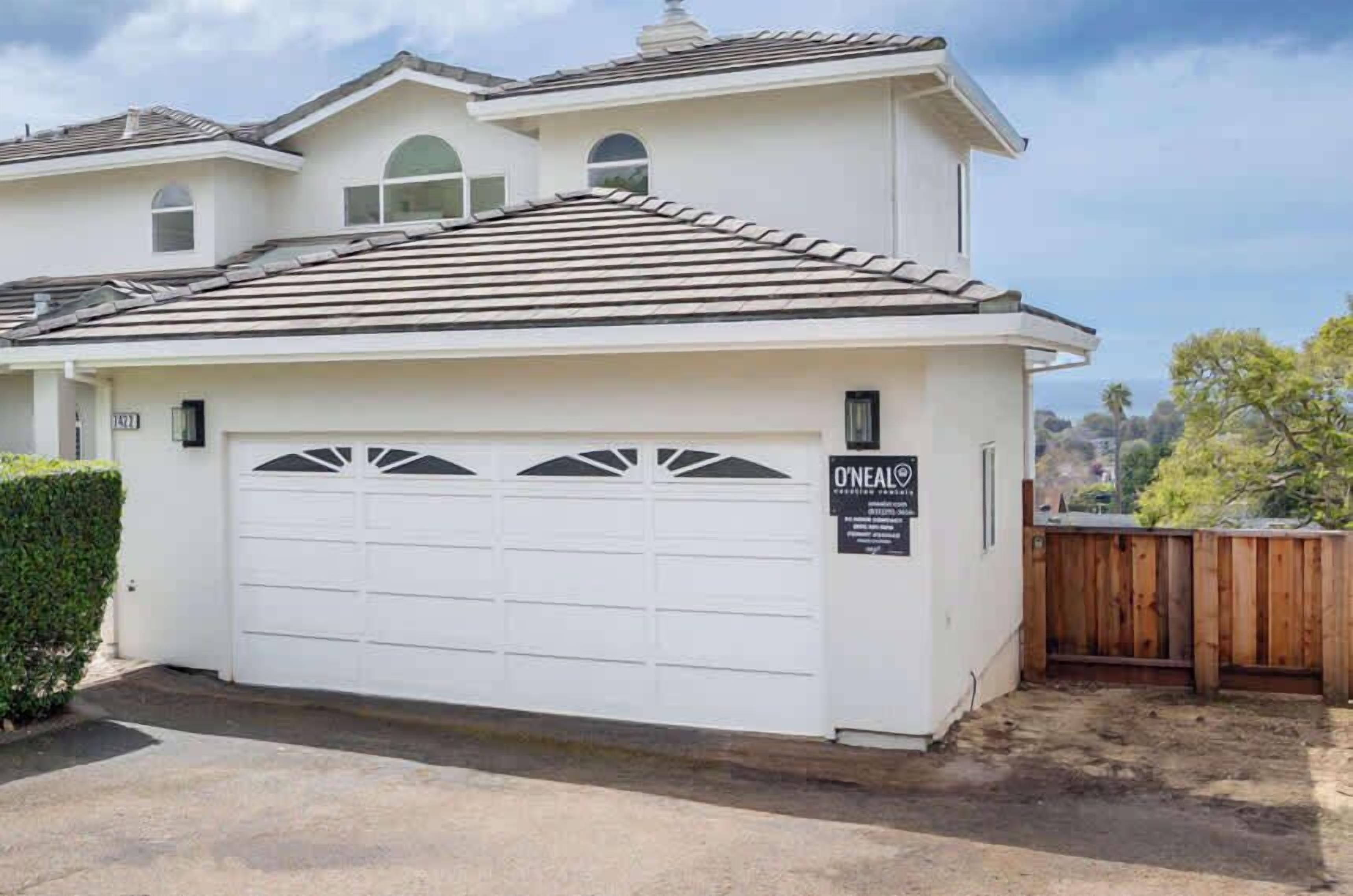 A single-story house with a white garage door, a sign indicating O'Neal's Real Estate, and a wooden fence in the background.