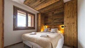 A bedroom with a wooden ceiling, a large window, and a bed with white linens and a beige blanket. - 6-person flat in a new residence on the snow front (LA TOUSSUIRE)