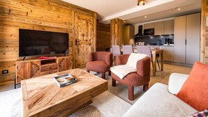 A modern living room with a wooden accent wall, a flat-screen TV, a coffee table, and seating. - 6-person flat in a new residence on the snow front (LA TOUSSUIRE)