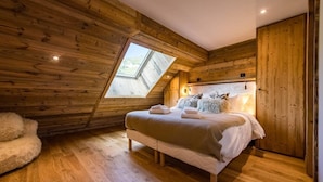 A bedroom with a sloped ceiling, wooden walls, a large bed with pillows, and a skylight. - 12-person flat with jacuzzi and sauna on the snow front (LA TOUSSUIRE)