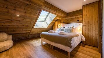 Une chambre avec un plafond en pente, des murs en bois, un grand lit avec des oreillers et une lucarne.