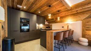 A modern kitchen with dark cabinets, a wooden island, and bar stools. - 12-person flat with jacuzzi and sauna on the snow front (LA TOUSSUIRE)