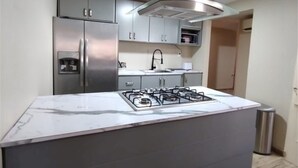 Une cuisine moderne dotée d’un îlot central, d’appareils électroménagers en acier inoxydable et de meubles de couleur grise.