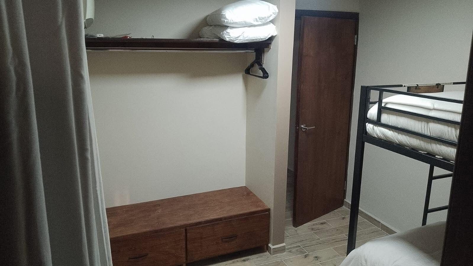 A bedroom with a bunk bed, a wooden bench, a wardrobe, and a curtain partially drawn.