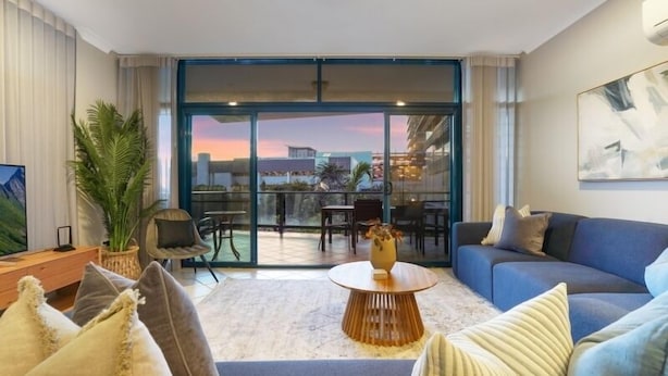 A modern living room with a sofa, a coffee table, and a large window with a city view. - Convenient CBD Location, Pool/Gym + walk to shops (Darwin)