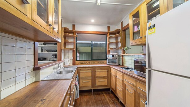 Eine kleine Küche mit Holzausstattung, einem Edelstahlspülbecken und einem weißen Kühlschrank.
