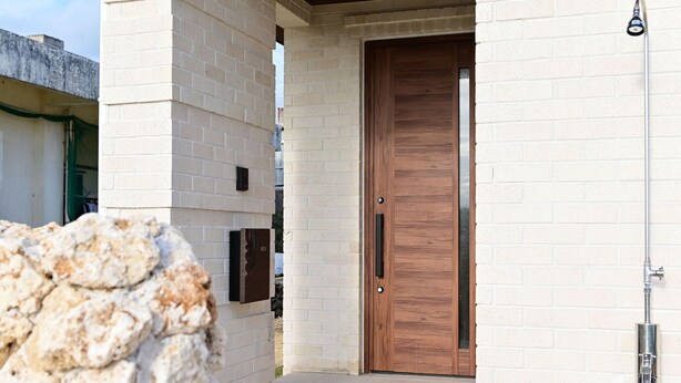 Ingresso di un edificio moderno con una porta in legno, una parete in pietra e un tubo di metallo.