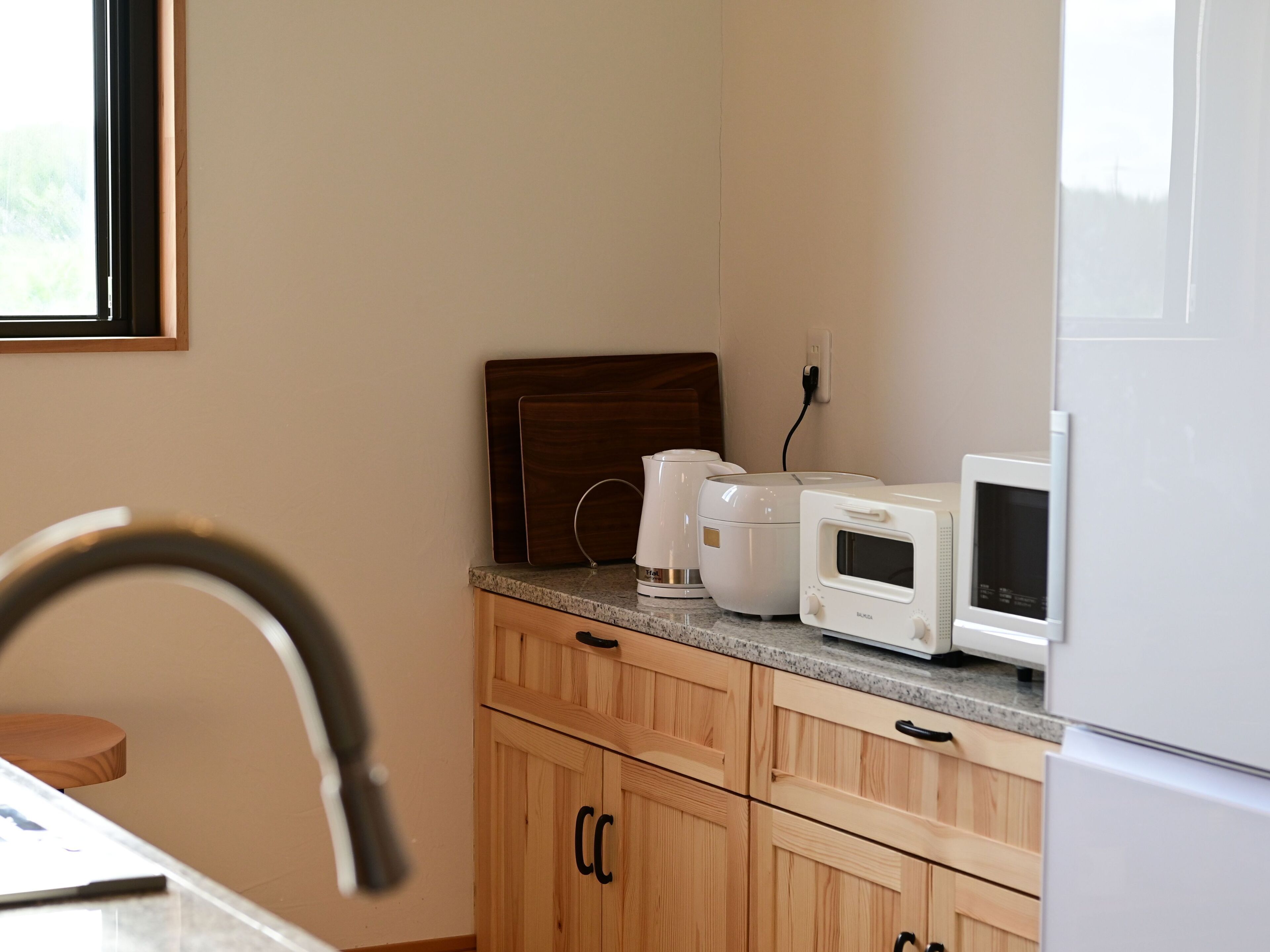 A kitchen with wooden cabinets, a countertop, a coffee maker, a rice cooker, and a microwave.