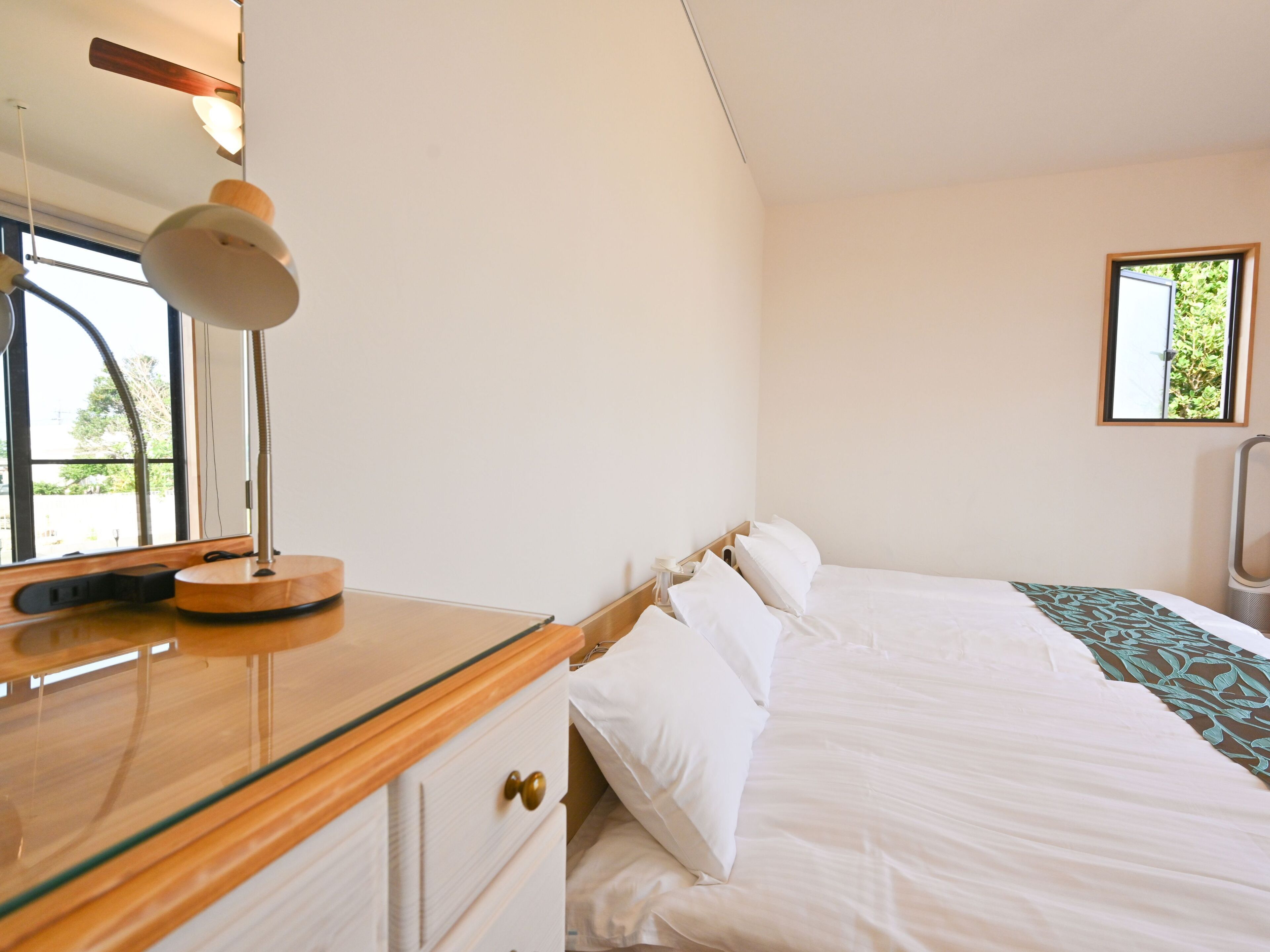 A bedroom with a bed, a bedside table with a lamp, a mirror, and a window.