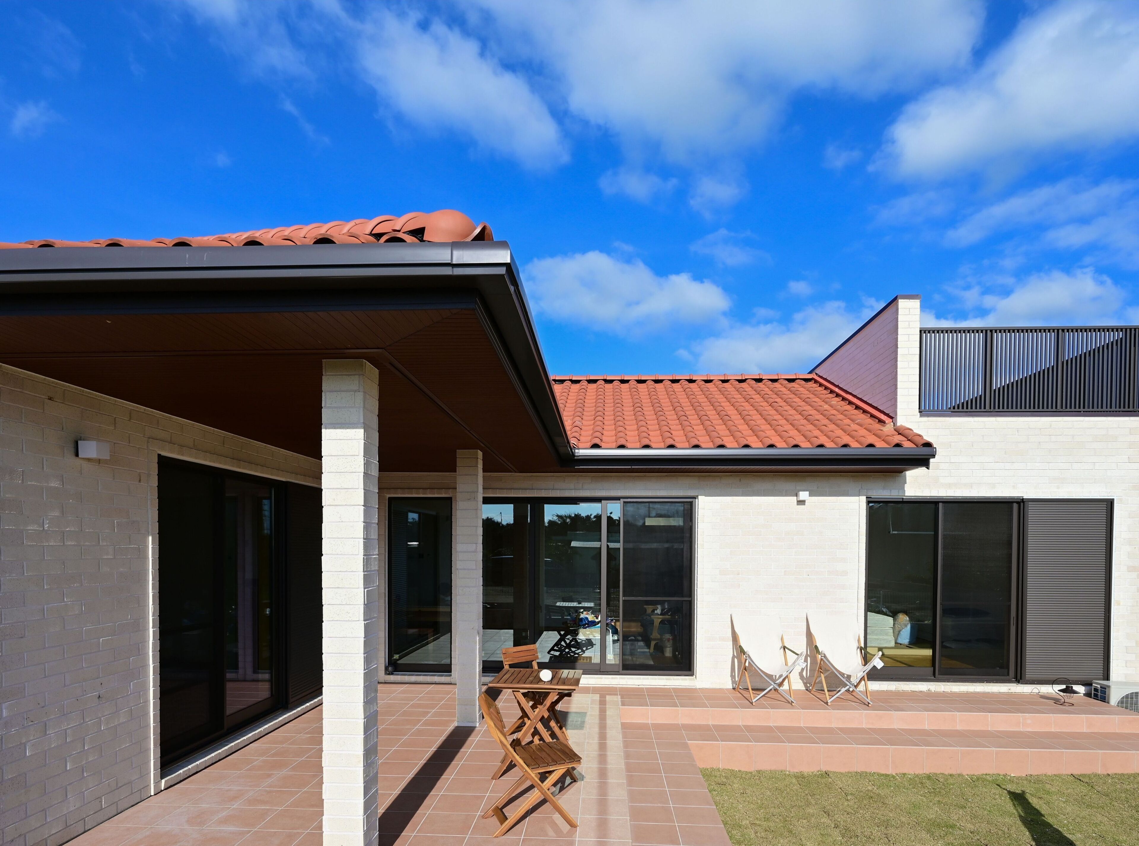 Une maison moderne dotée d’un patio couvert, de grandes fenêtres et d’un toit recouvert de tuiles rouges.