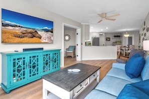 A living room with a teal cabinet, a gray coffee table, a blue sofa, and a kitchen in the background.