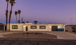 A modern two-story house with a garage, a driveway, and a landscaped front yard with palm trees. - Poolside Retreat with Firepit & Game-Ready Fun (Lake Havasu City)