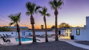 Un jardin avec une piscine, des palmiers, des chaises longues et un petit espace patio.
