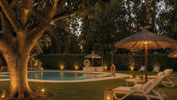 A pool area with lounge chairs, a thatched umbrella, and a tree. - Las Terrazas 2 | Modern Golf Terrace Pool (Benahavís)