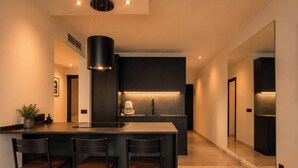 A modern kitchen with a central island, bar stools, a coffee machine, and a large mirror. - Las Terrazas 2 | Modern Golf Terrace Pool (Benahavís)