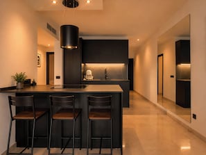 A modern kitchen with a central island, bar stools, a coffee machine, and a large mirror.