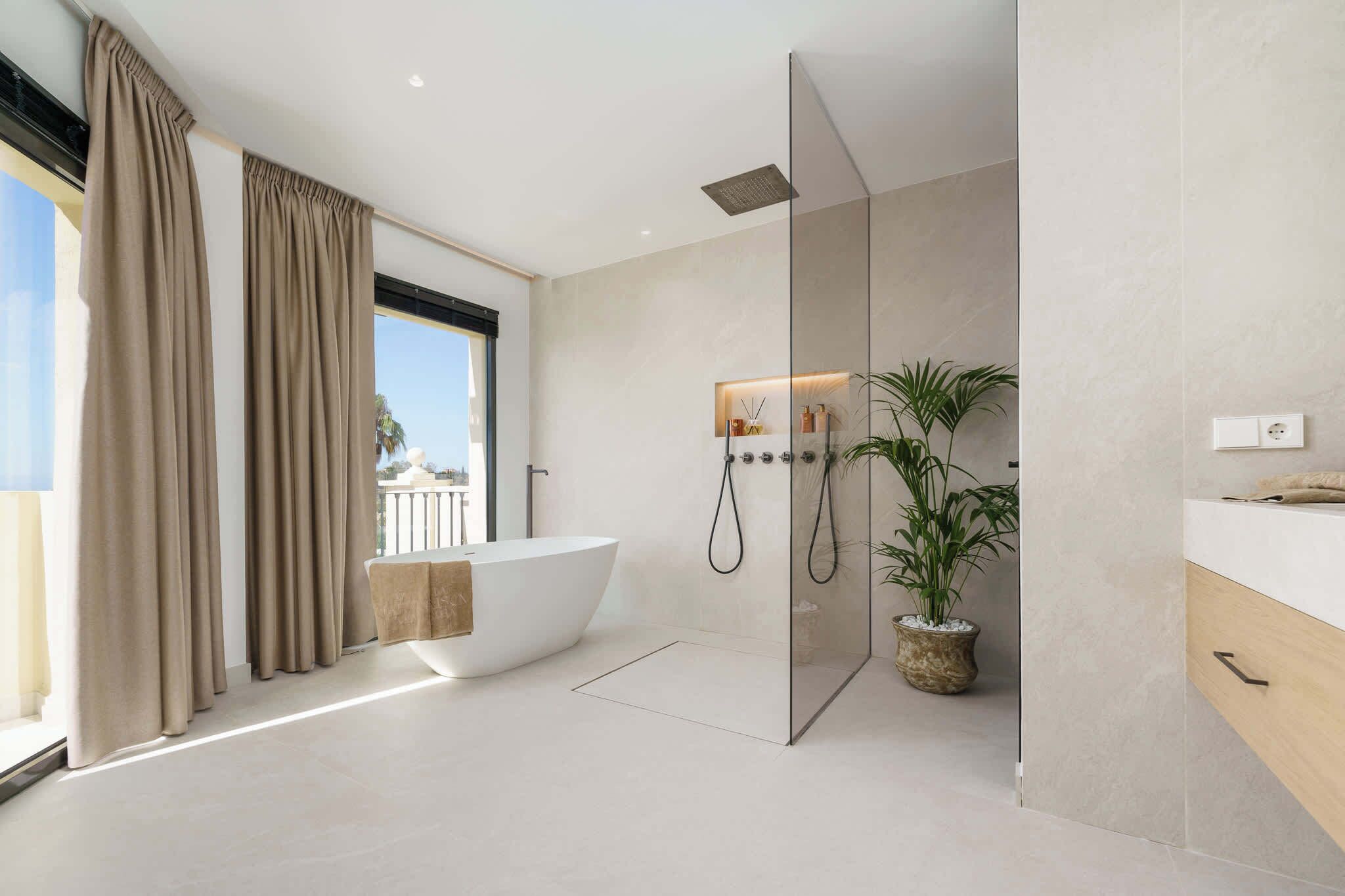 A modern bathroom with a freestanding bathtub, a glass-enclosed shower, and a potted plant.