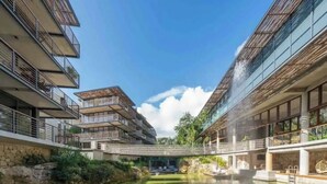 Un edifici modern amb múltiples balcons, una font central i una paret de pedra.