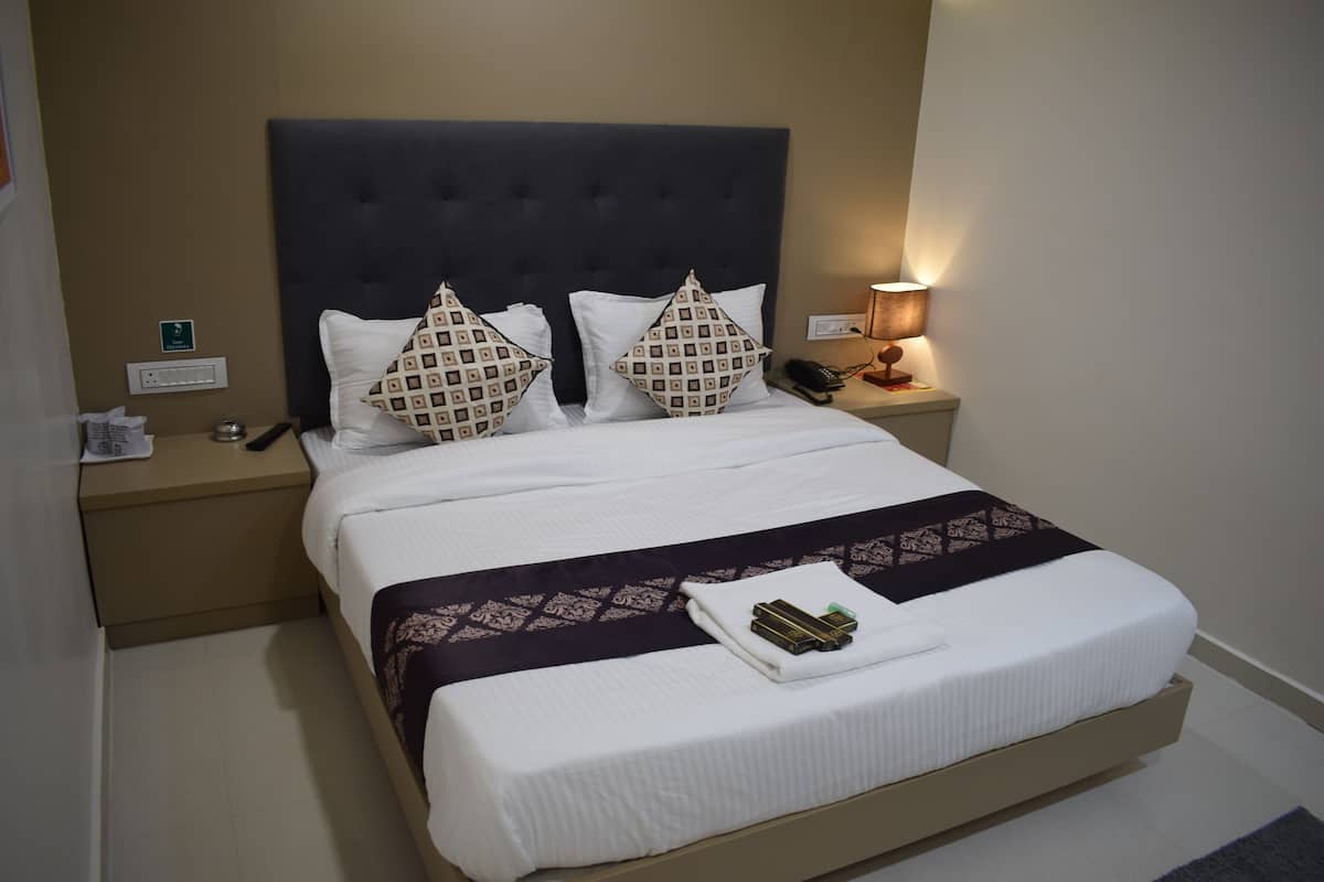 A neatly made bed with a dark headboard, two patterned pillows, a white blanket, and a bedside table with a lamp and a phone.