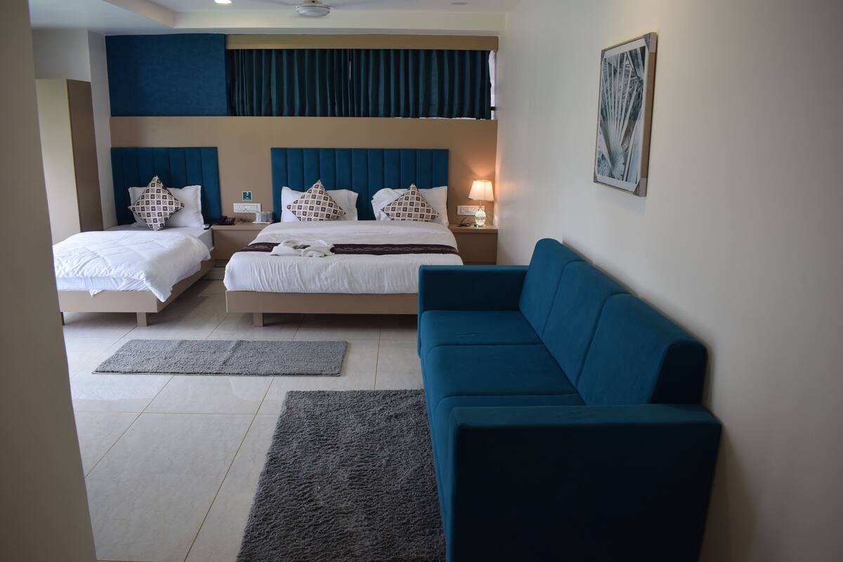 A hotel room with two beds, a blue sofa, a small table, and a wall-mounted artwork.
