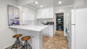 Een moderne keuken met witte kasten, een centraal eiland met krukken, een magnetron en een inbouwoven.
