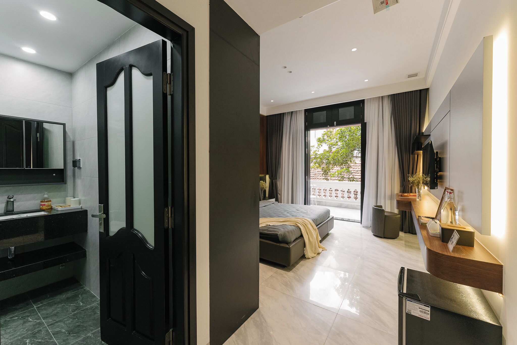 Habitació d'hotel moderna amb bany, un llit, escriptori i una finestra gran.