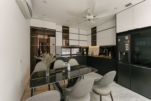 A modern kitchen with a black and white color scheme, a glass dining table, and a built-in oven. - Tamundi Alley Homestay - Dragon Teeth - The Old Quarter Ha Noi (Hanoi)