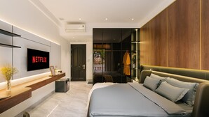 Une chambre à coucher moderne avec un grand lit, un téléviseur fixé au mur et une armoire en bois.