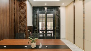 Une salle de conférence avec une table en bois, des chaises, une plante en pot et une porte noire dotée de panneaux de verre.