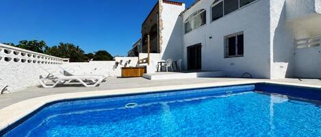 A clear blue pool with a white building in the background, a wooden bench, and a white fence.