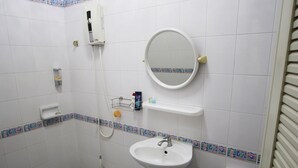 A bathroom with a white sink, a round mirror, a handheld showerhead, and a small shelf with toiletries.