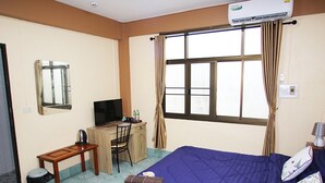 A hotel room with a bed, a desk, a chair, a television, and an air conditioning unit.