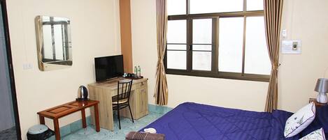 A hotel room with a bed, a desk, a chair, a television, and an air conditioning unit.
