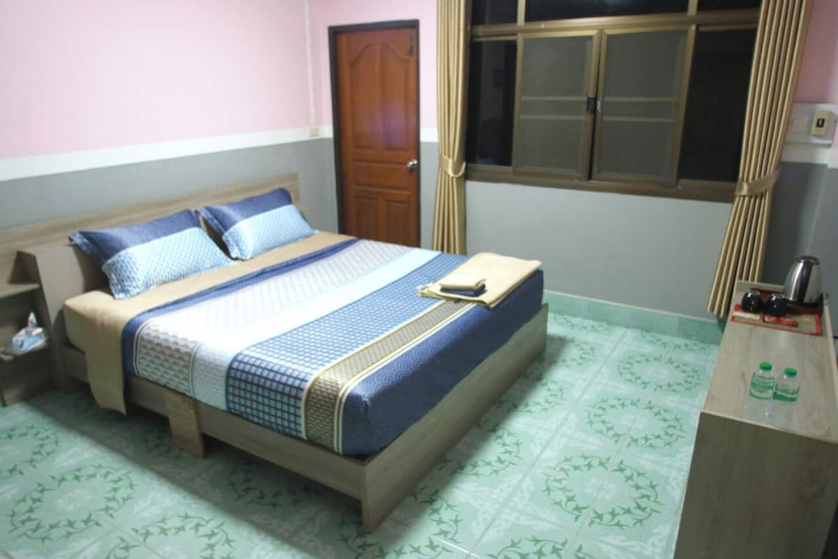 Una cama individual con una colcha estampada, un cabecero de madera y una mesita de noche con una botella y una taza.