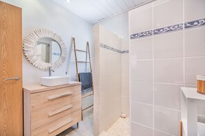 Ein Badezimmer mit einem Holzbadezimmermöbel, einem Spiegel, einem Handtuchhalter und einem Duschbereich mit gefliesten Wänden.