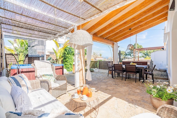 A covered outdoor seating area with wicker furniture, a table with drinks, and a potted plant.