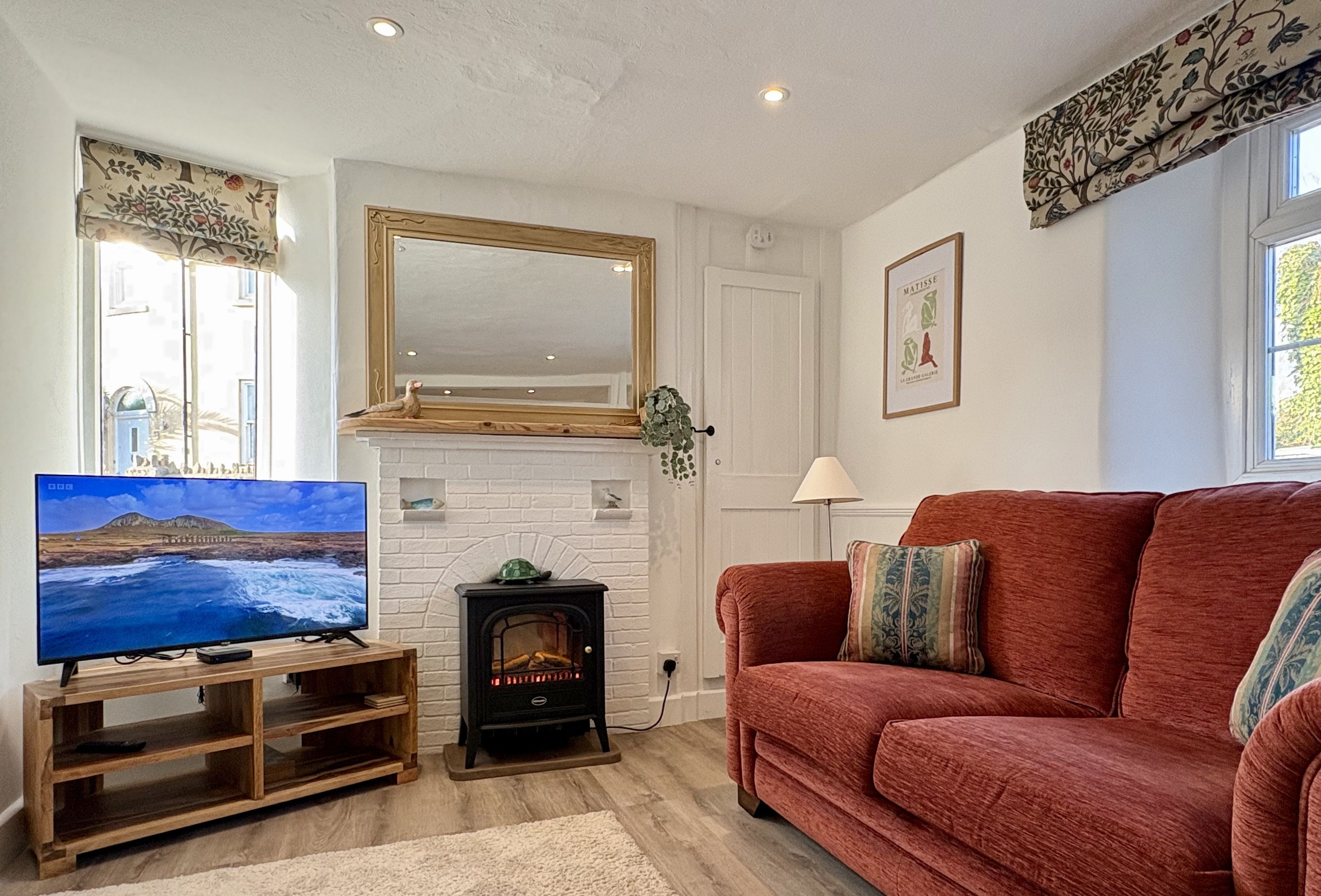 Ein Wohnzimmer mit Fernseher auf Holzständer, einem roten Sofa, einem Kamin und einem großen Spiegel an der Wand.